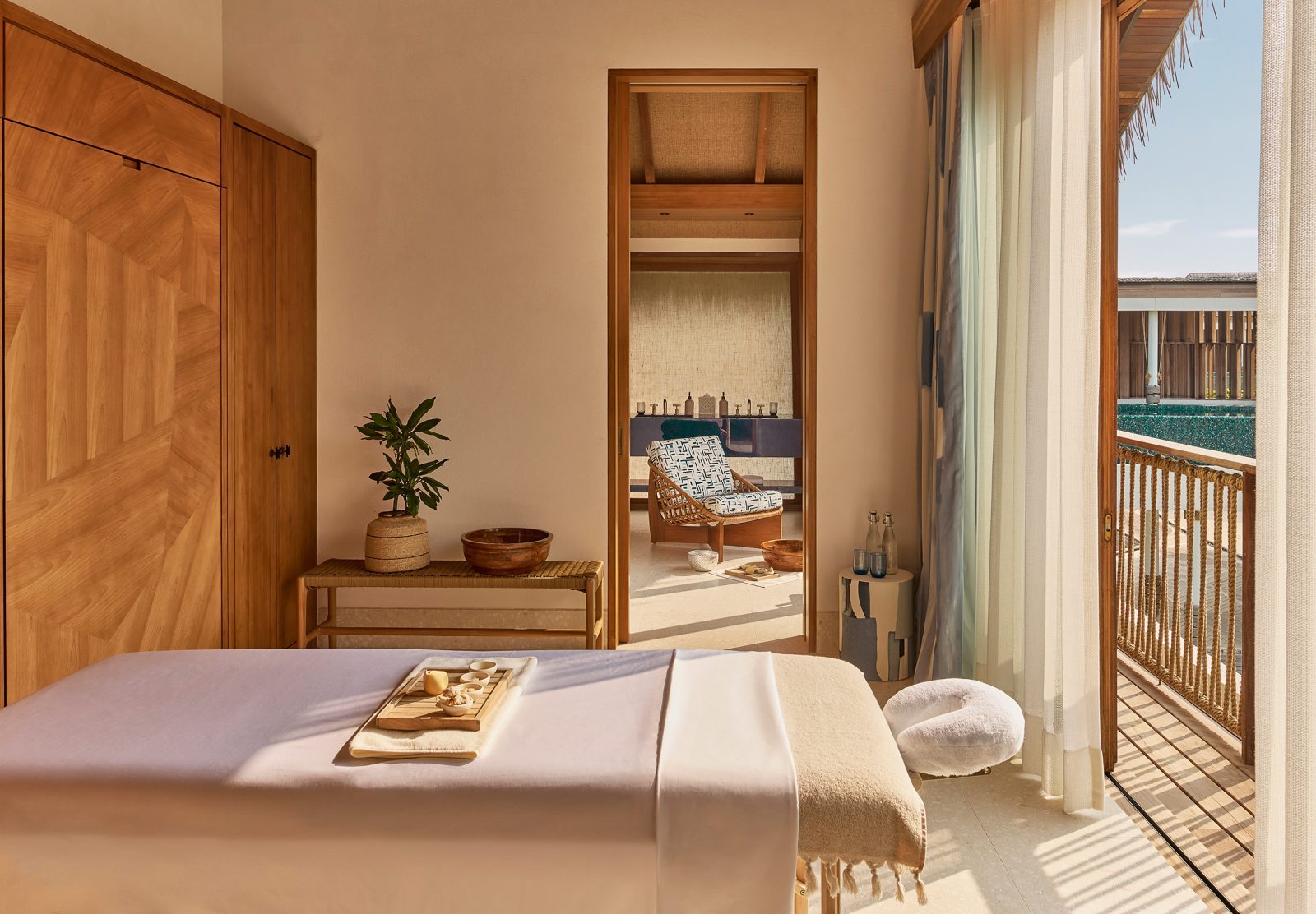 Schlafzimmer mit Bett und Holzmöbeln, Blick durch Tür auf Balkon mit Pool, Lounge-Stuhl und Deko